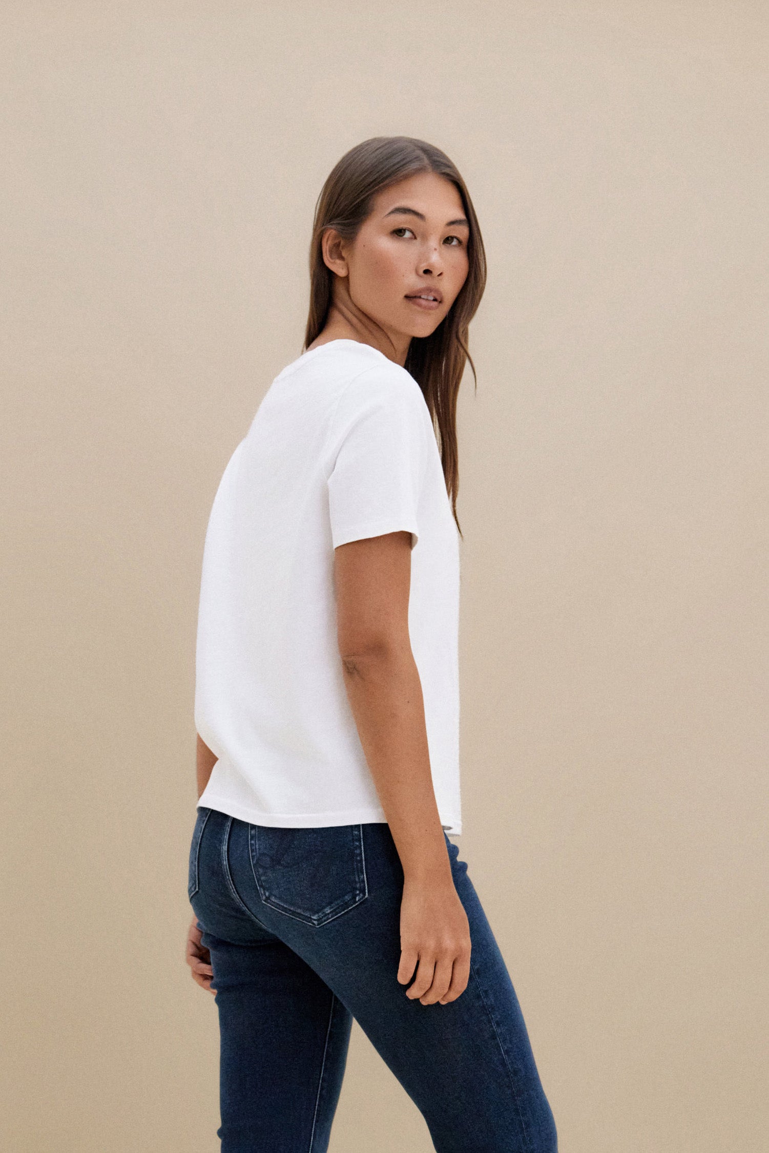 Woman wearing a plain white t-shirt and blue jeans against a beige background