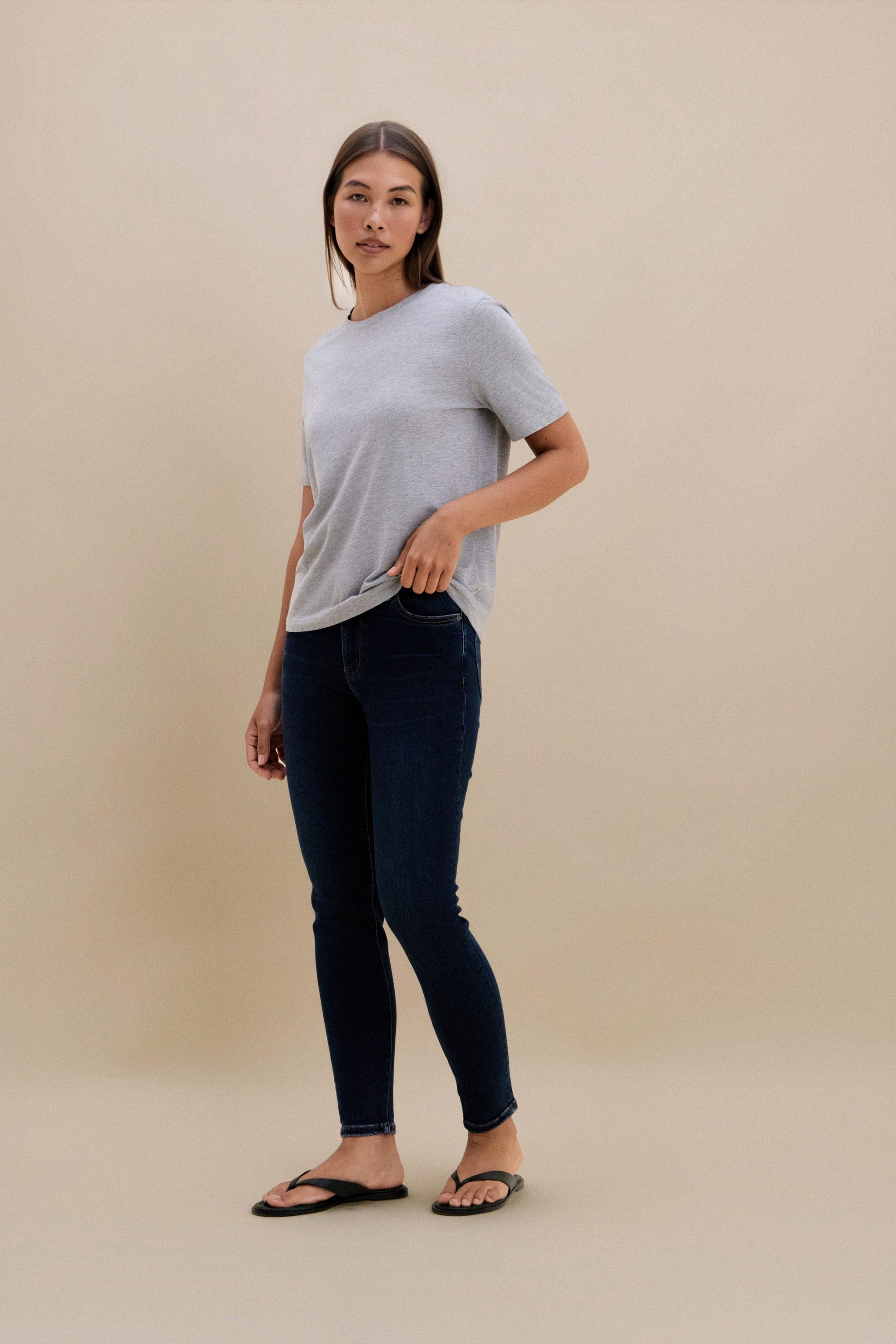 Woman wearing a gray t-shirt and dark jeans on a beige background