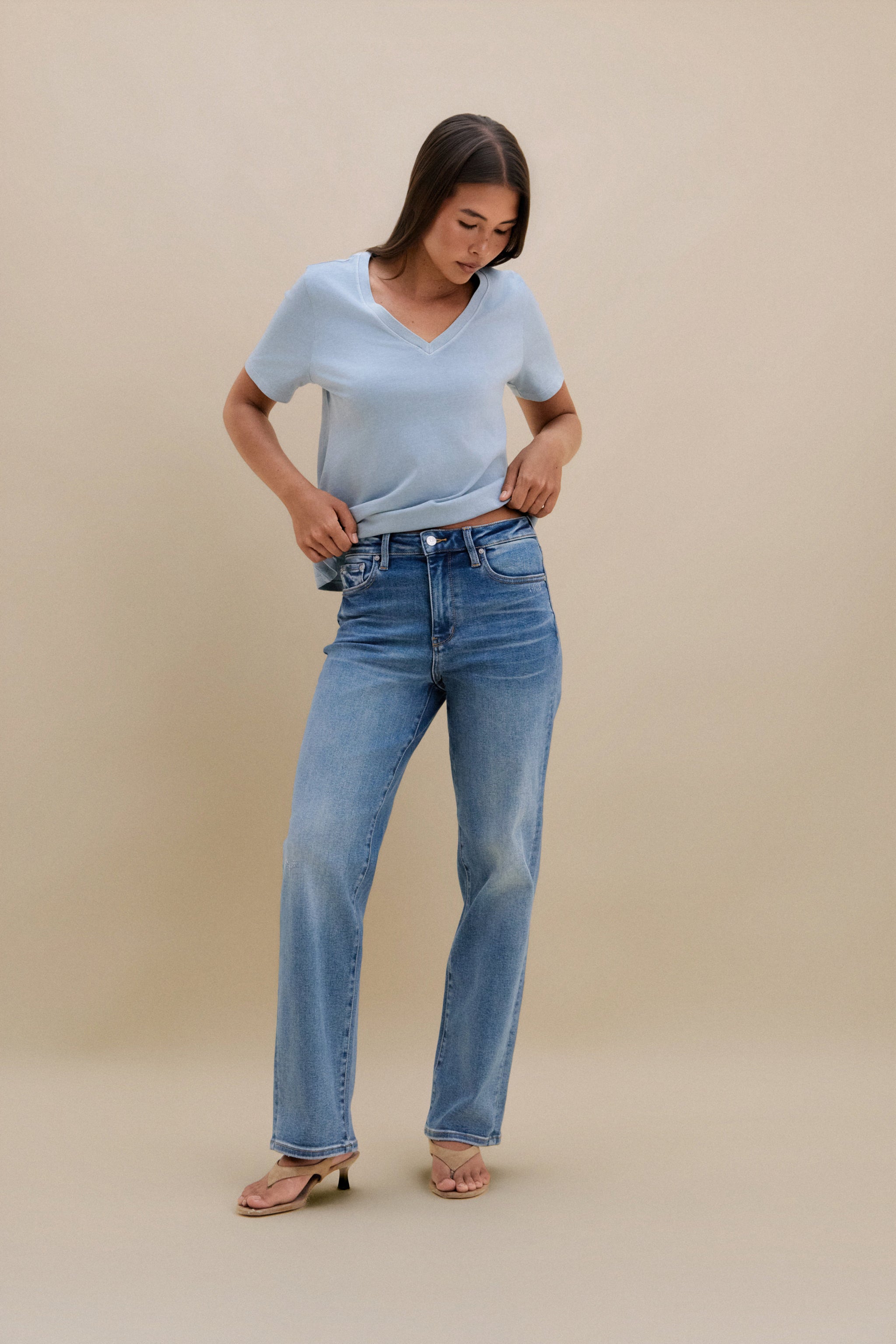 Woman wearing a light blue t-shirt and blue jeans against a beige background