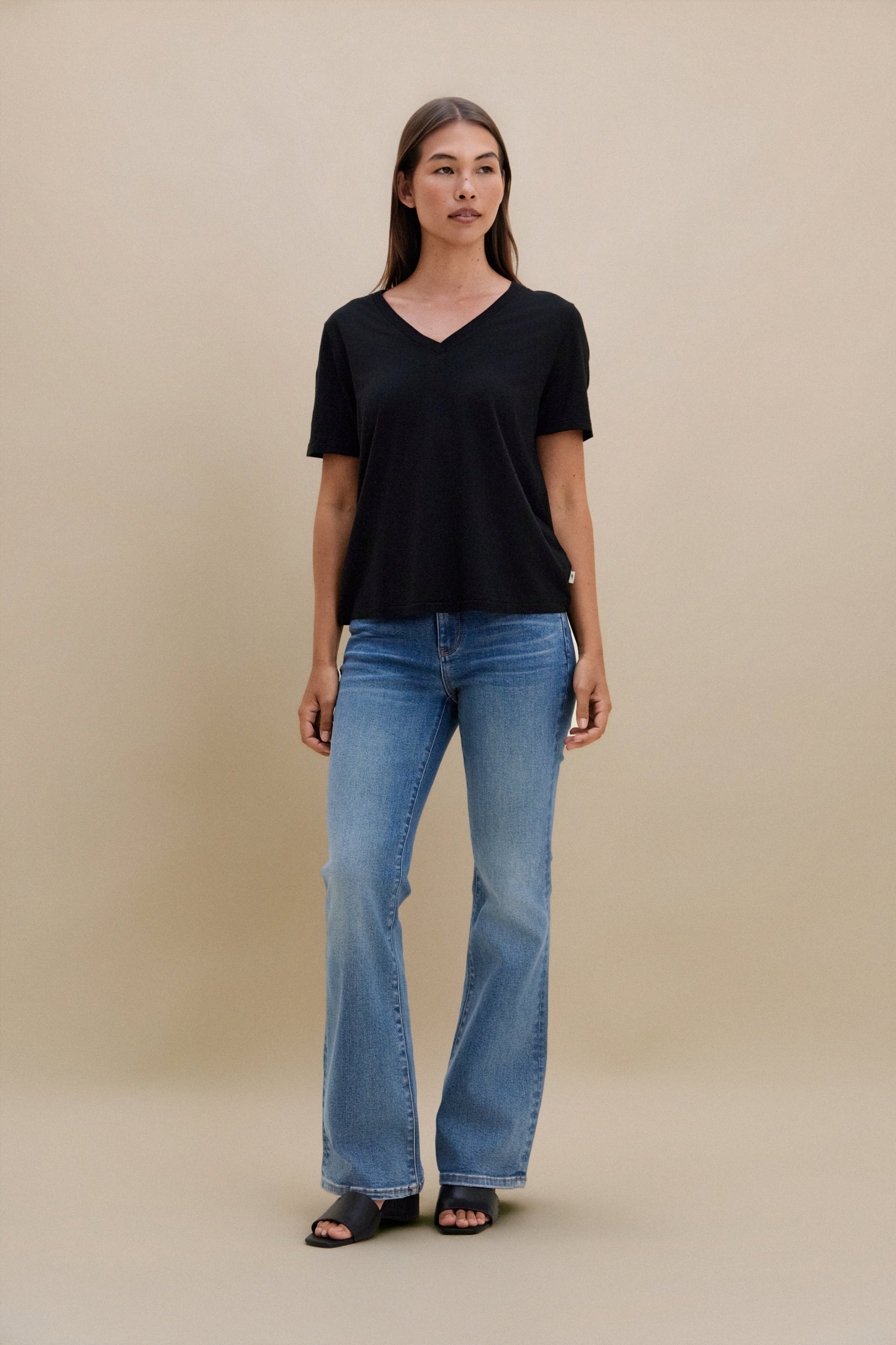 Woman wearing a black V-neck shirt and blue jeans against a beige background
