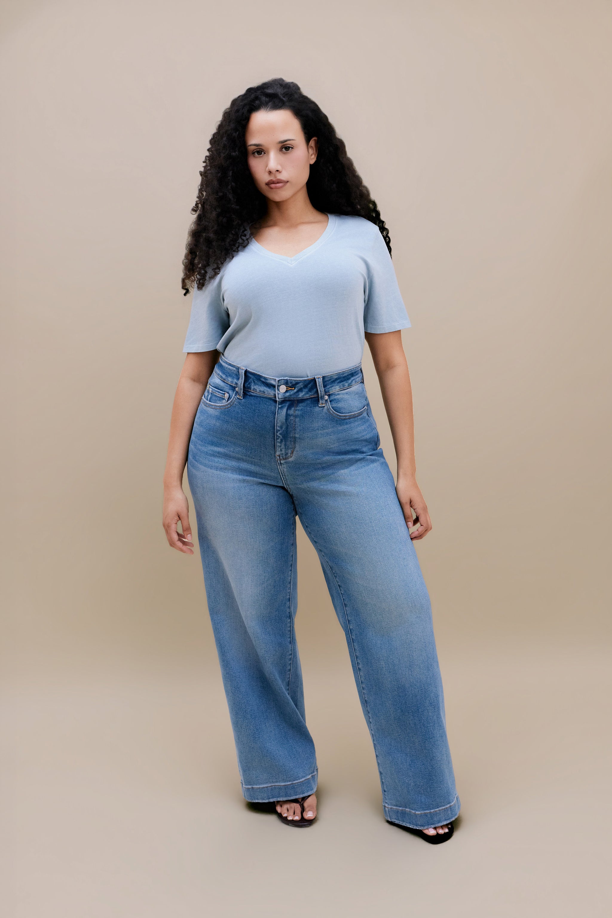Woman wearing a blue t-shirt and wide leg jeans with a beige background | model-size: 16