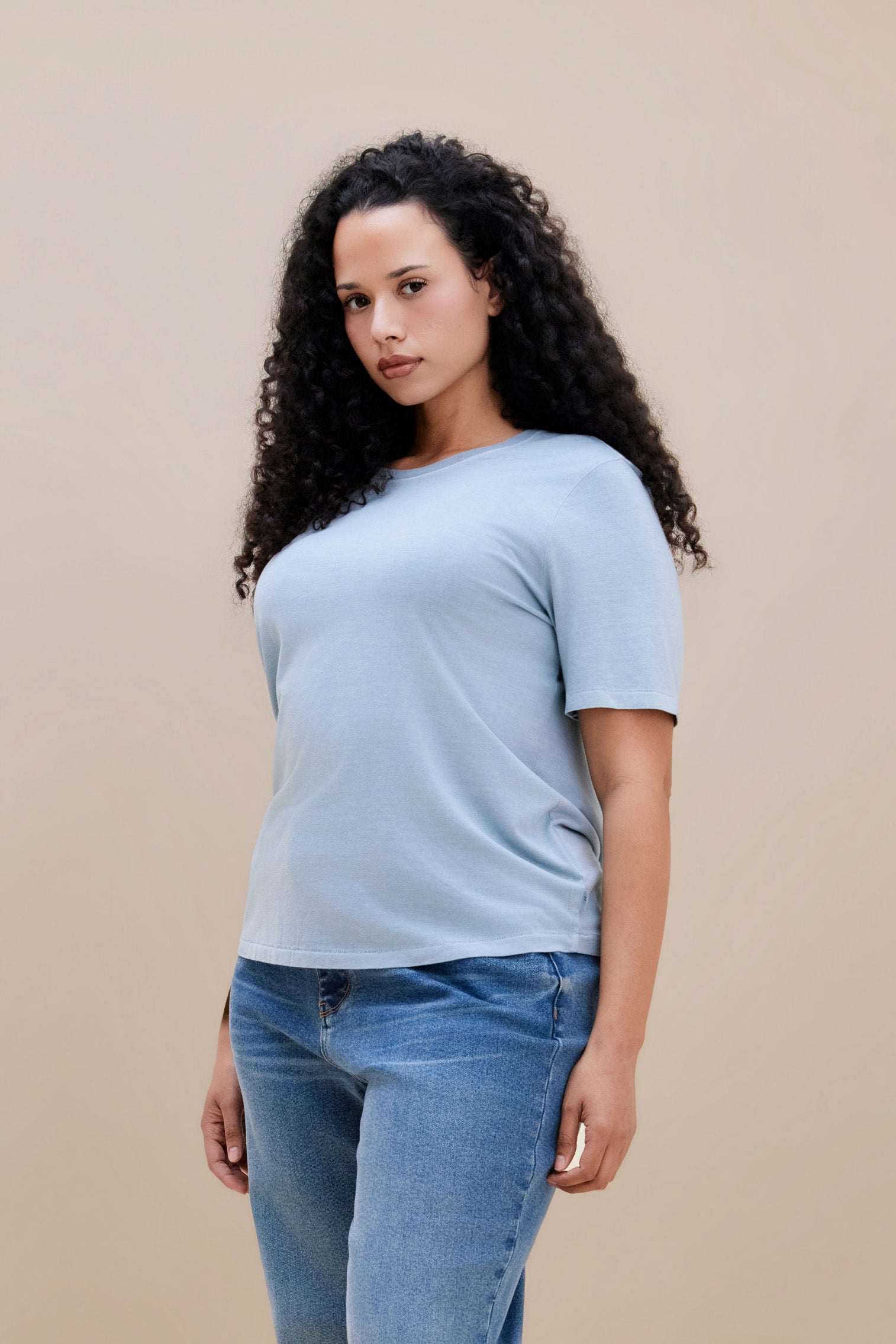 Woman wearing a light blue t-shirt and jean against a beige background