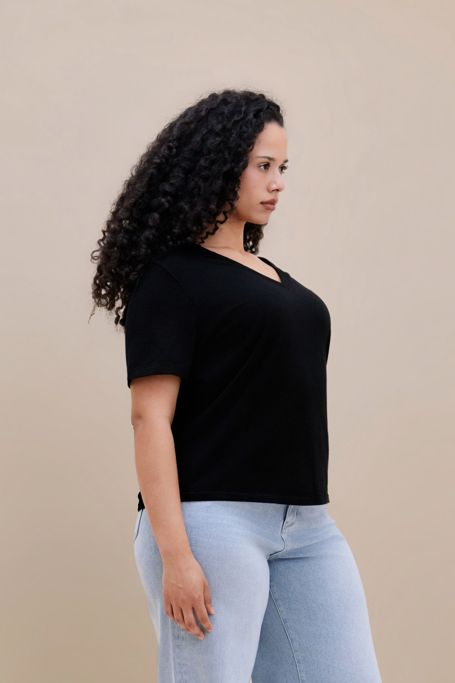 Woman wearing a black t-shirt and light blue jeans against a beige background