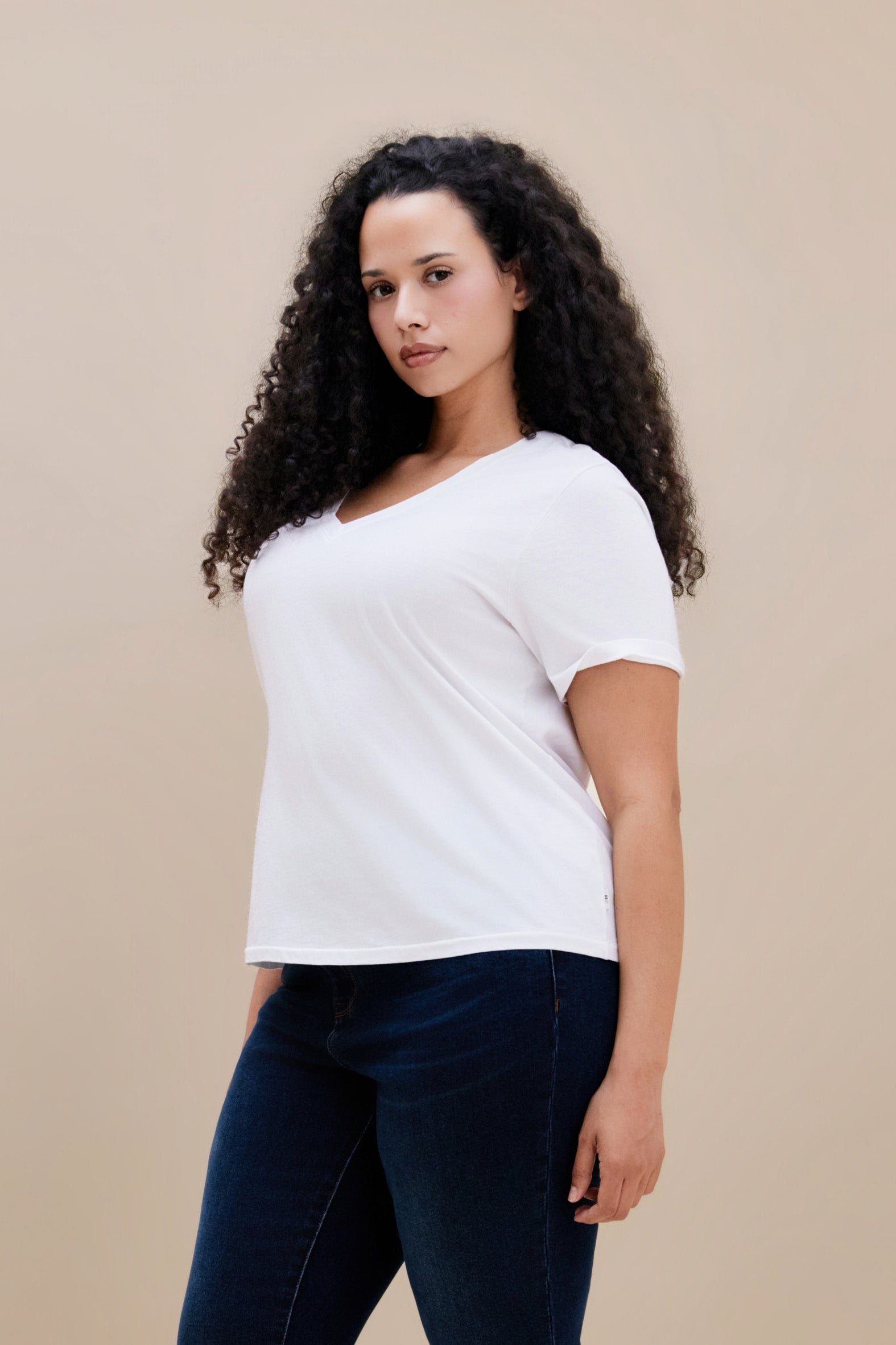 Woman wearing a plain white t-shirt and dark jeans against a beige background