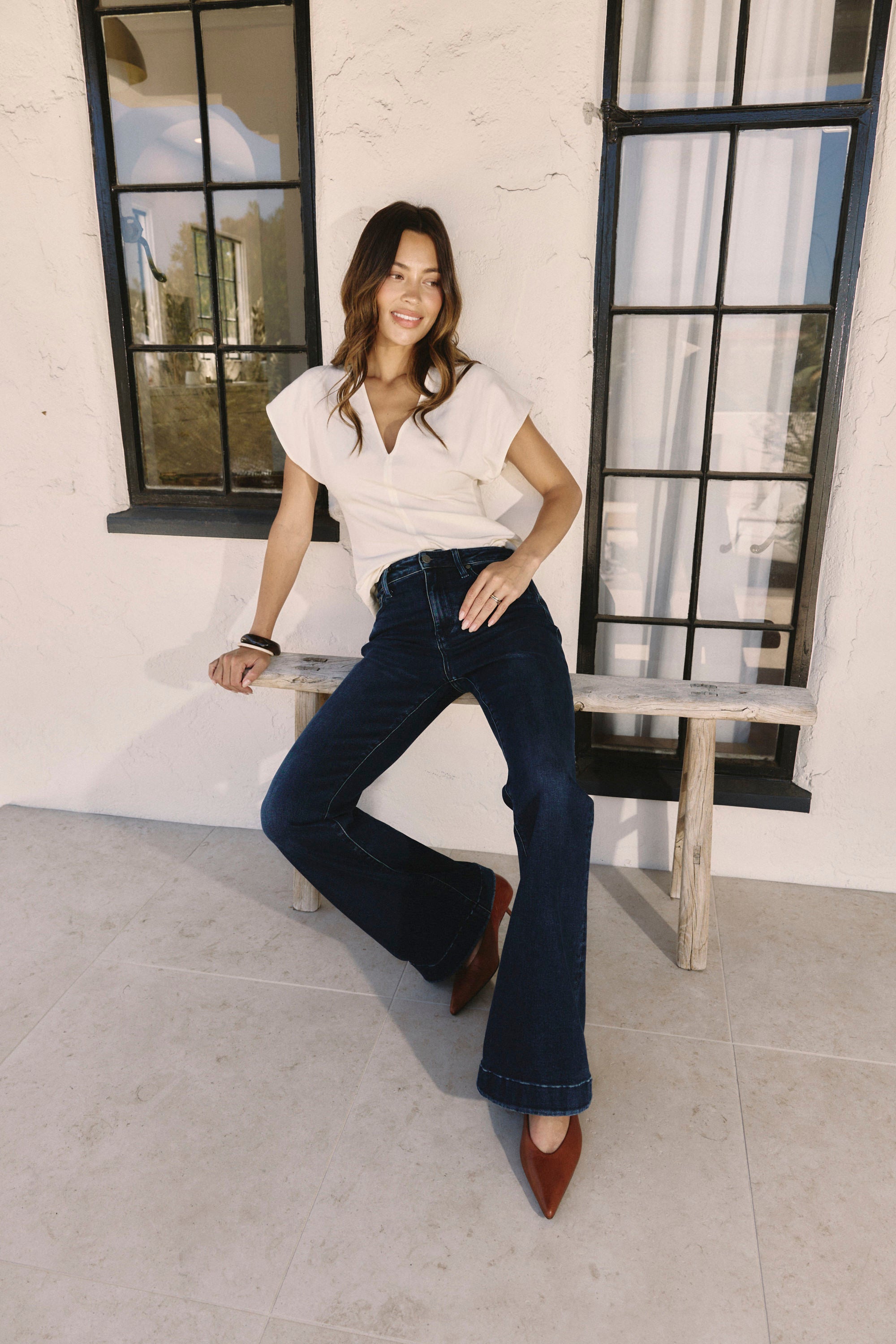 Woman sitting on a bench wearing a white top and blue jeans in a bright outdoor setting | model-size: 4