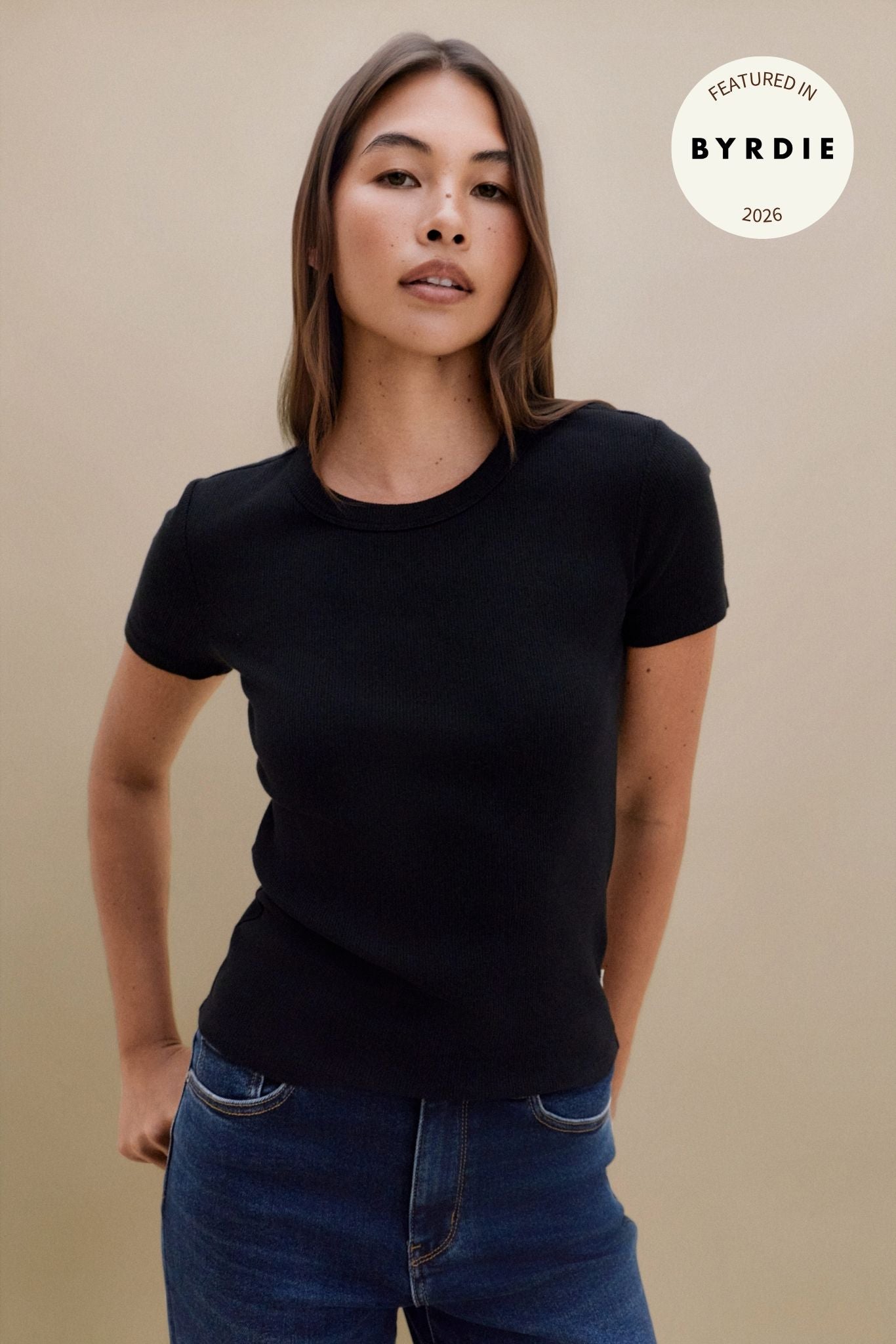 Woman wearing a black t-shirt and blue jeans with a Byrdie logo in the corner | model-size: 4