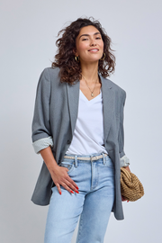 Woman wearing a gray blazer, white shirt, and light blue jeans against a plain background | model-size: 4