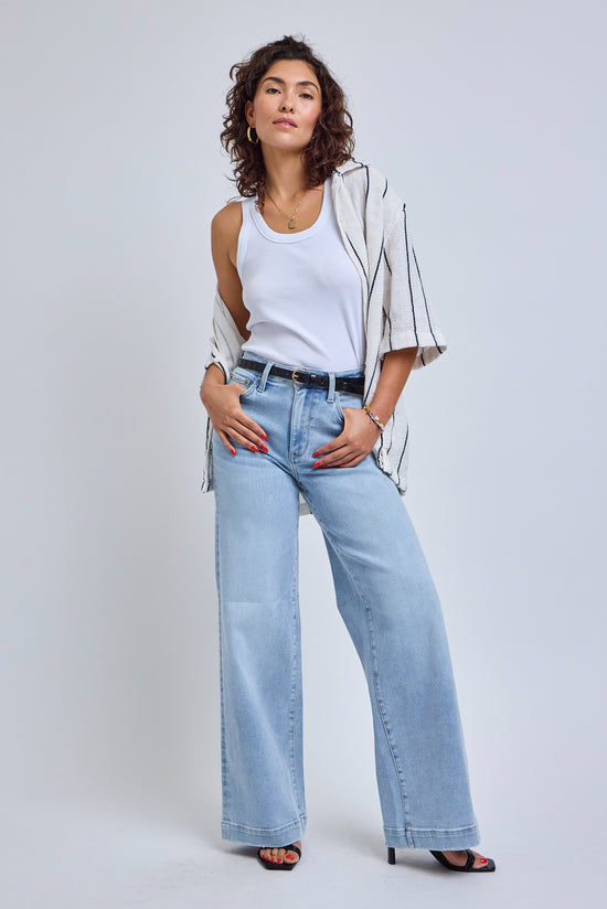 Woman wearing a white top, beige jacket, and light blue jeans on a white background | model-size: 4