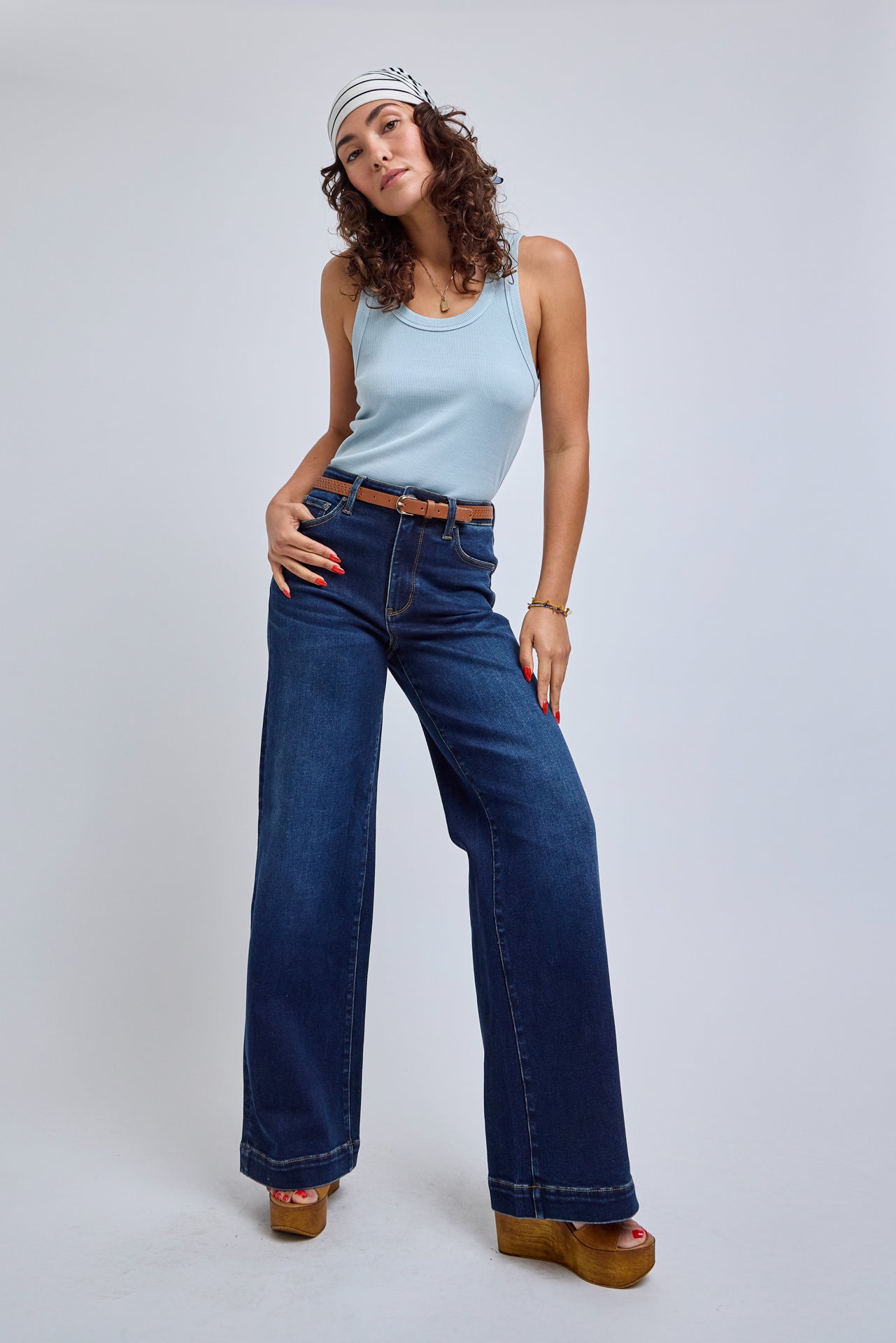 Woman wearing a light blue sleeveless top and dark blue jeans on a white background | model-size: 4