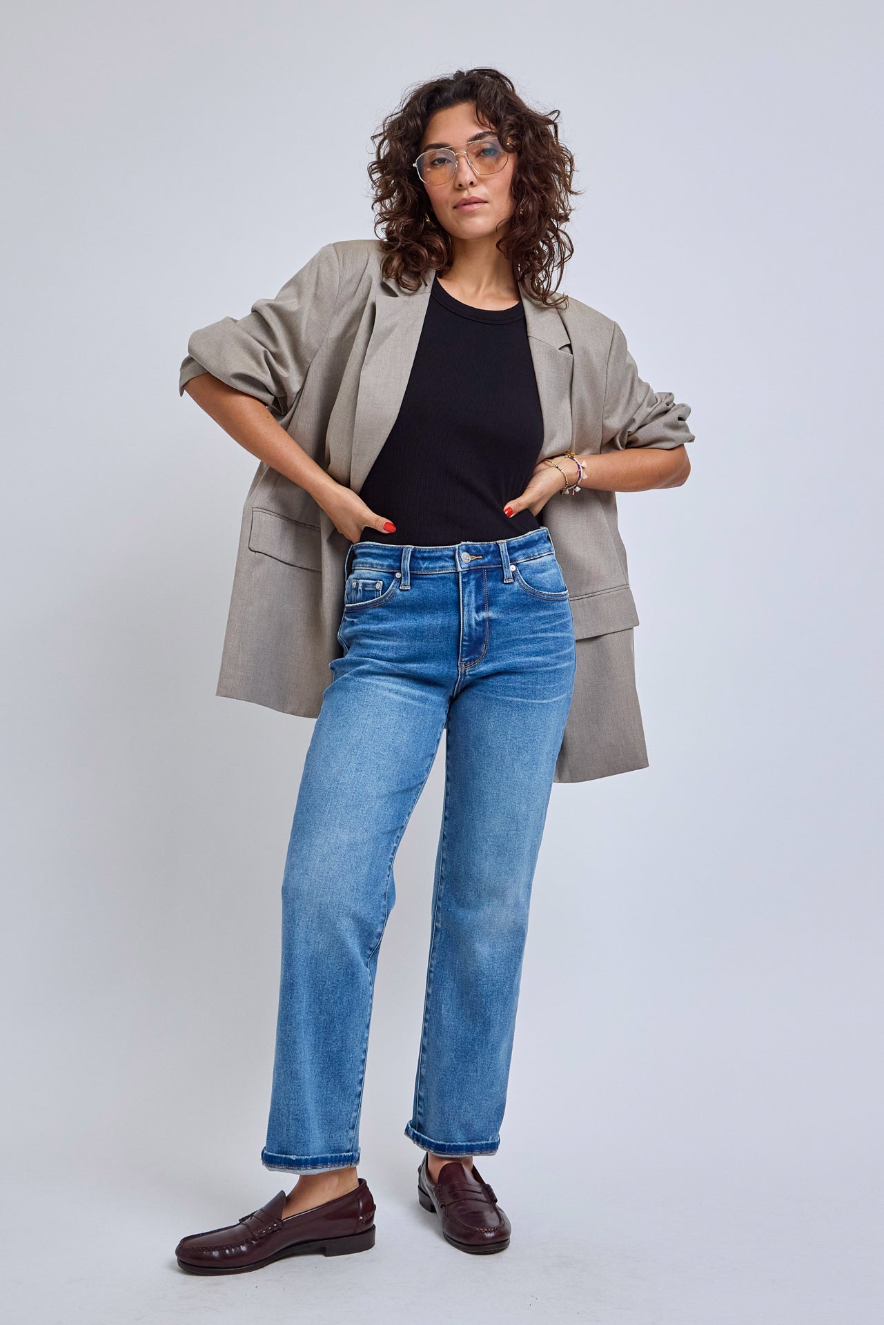 Woman wearing a beige blazer, black top, blue jeans, and brown shoes on a white background | model-size: 4