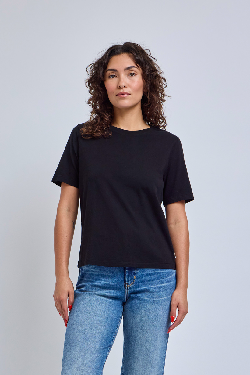 Woman wearing a black crew neck t-shirt and blue jeans standing in front of a gray wall | model-size: 4