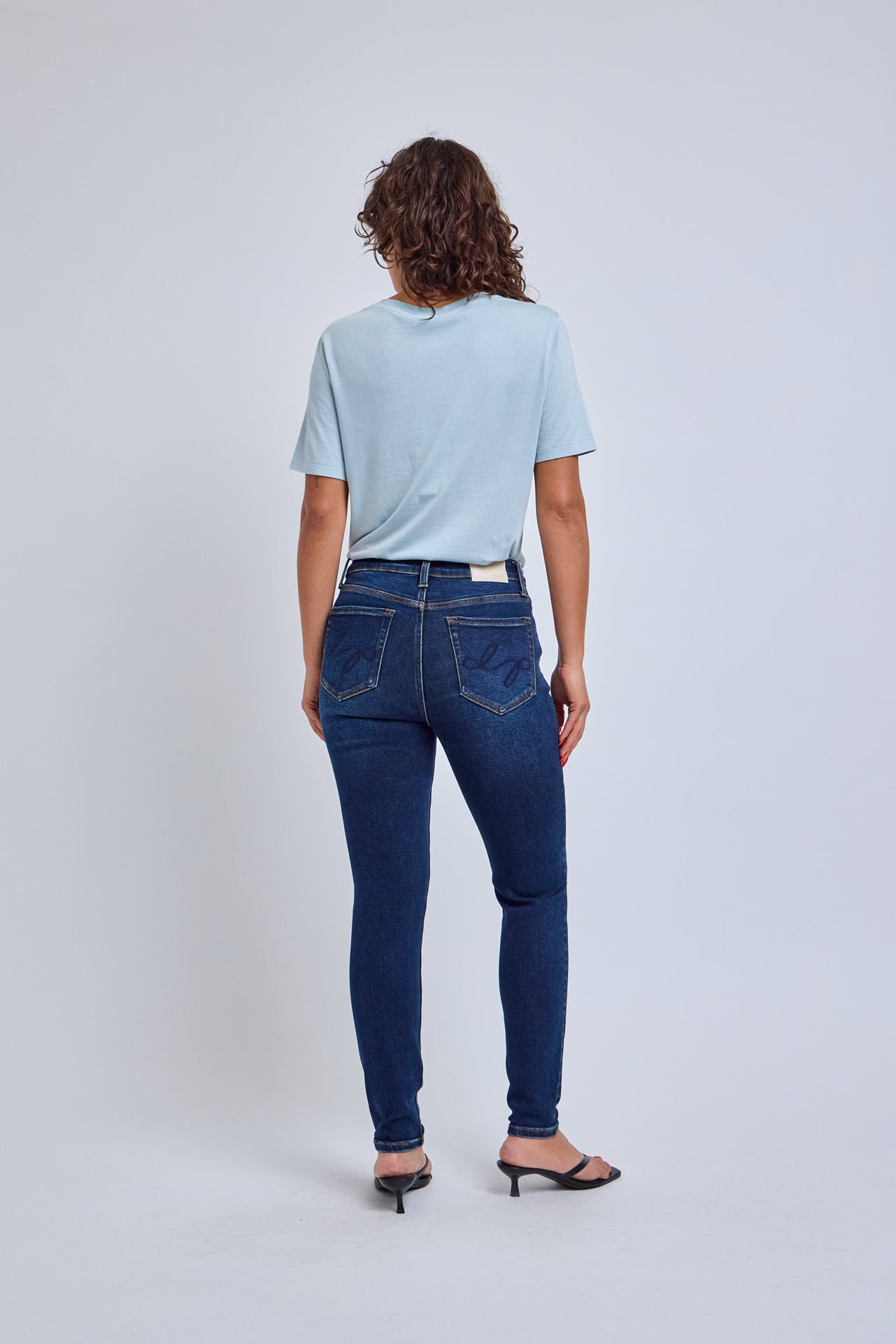 Woman wearing blue jeans and a light blue shirt on a white background