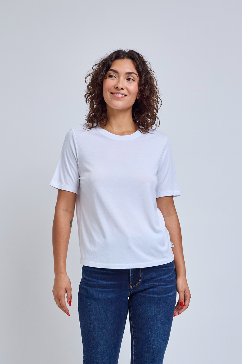 Woman wearing a crew neck white t-shirt and jeans against a gray wall | model-size: 4