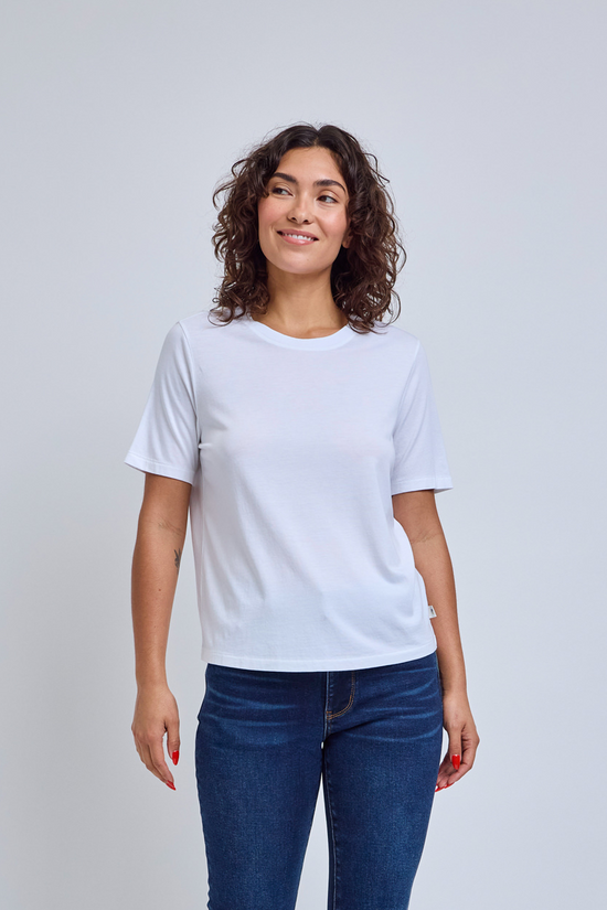 Woman wearing a crew neck white t-shirt and jeans against a gray wall | model-size: 4