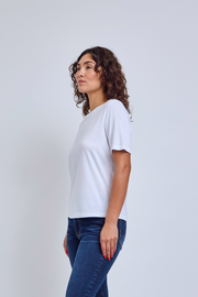 Woman wearing a white crew neck shirt and jeans against a gray wall