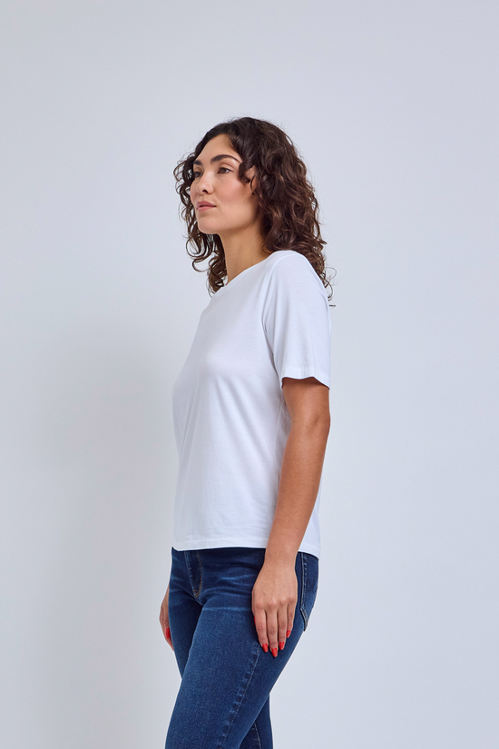 Woman wearing a white crew neck shirt and jeans against a gray wall