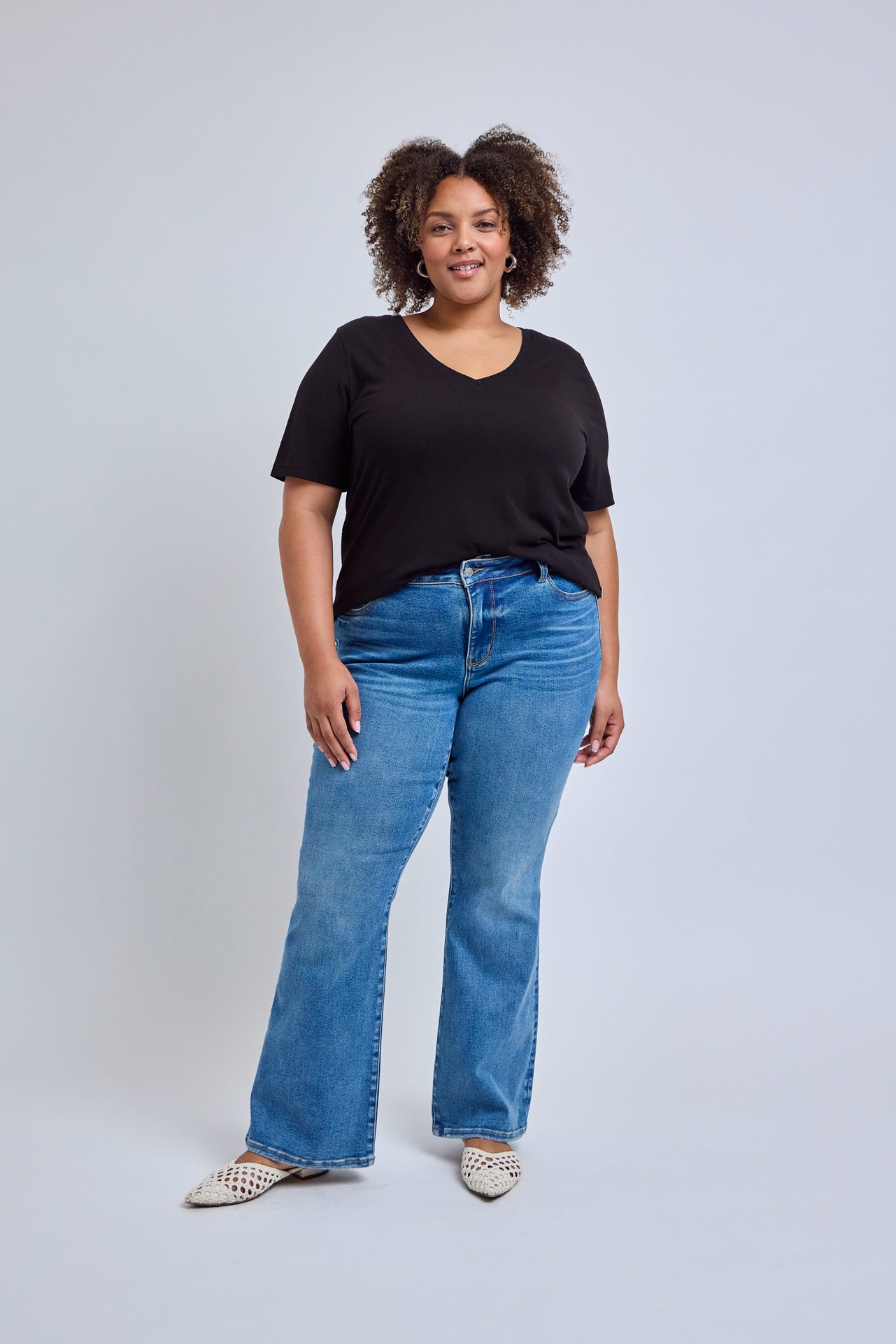 Woman wearing a black t-shirt and blue jeans on a light gray background 