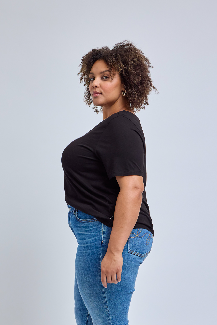 Woman wearing a black t-shirt and blue jeans against a light gray background