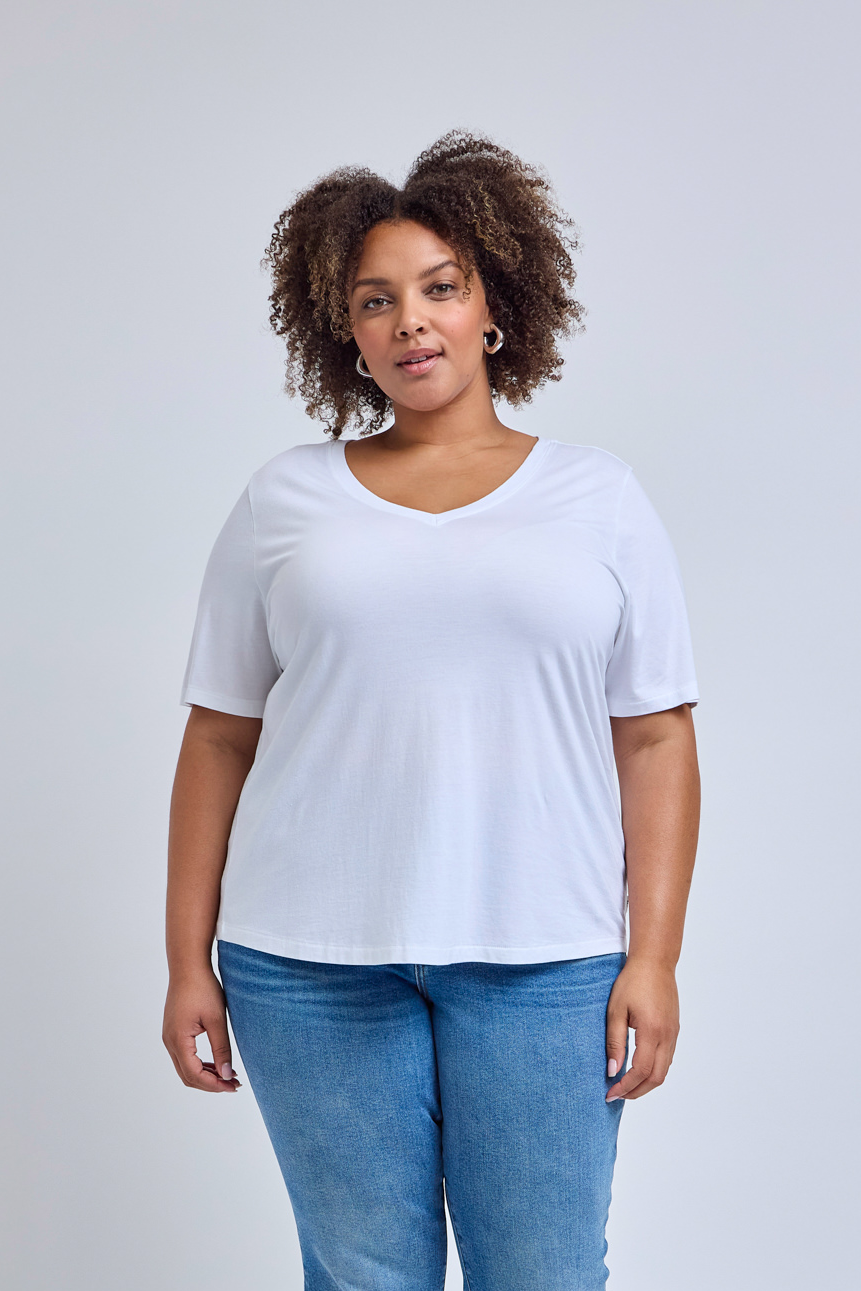 Woman wearing a white v-neck tee and jeans with a gray background | model-size: 16