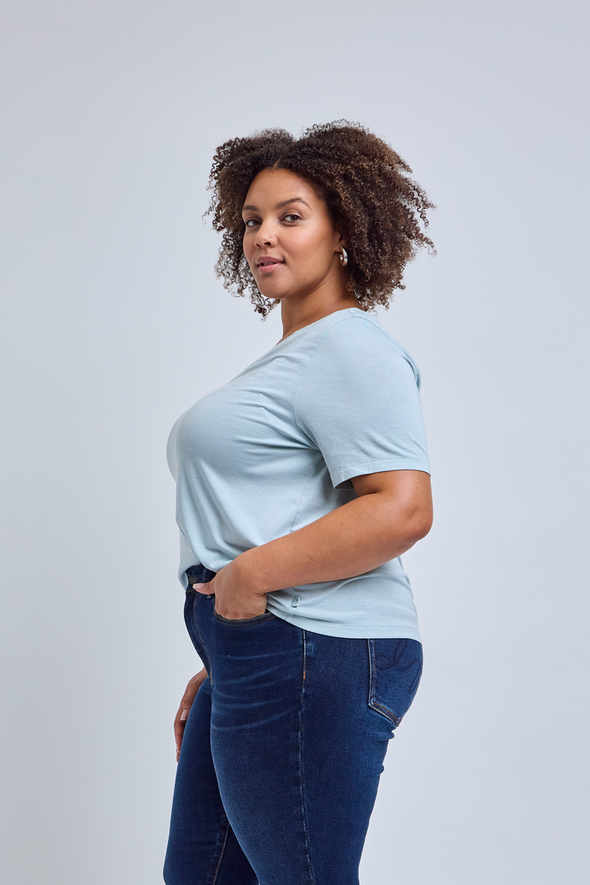 Woman wearing a light blue t-shirt and dark blue jeans against a gray background