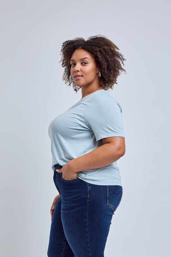 Woman wearing a light blue t-shirt and dark blue jeans against a gray background