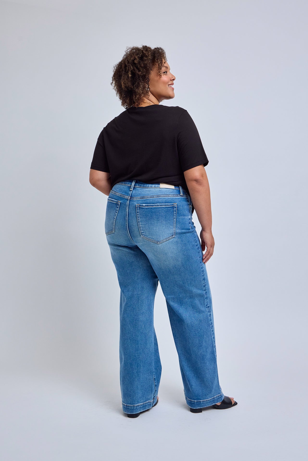 Person wearing blue jeans and a black top on a light gray background