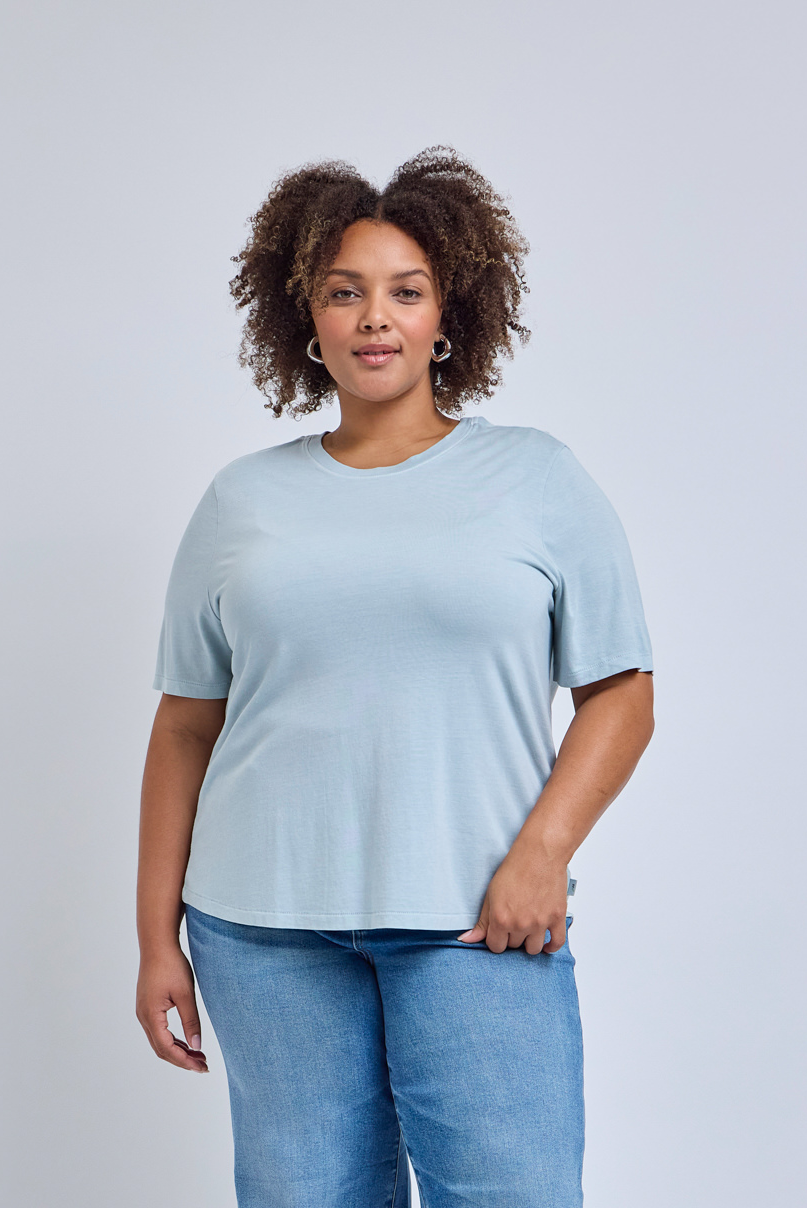 Woman wearing a light blue t-shirt and jeans against a plain background | model-size: 16