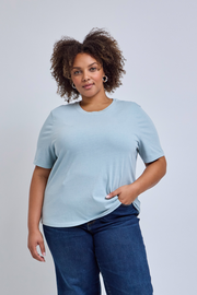 Woman wearing a light blue t-shirt and dark blue jeans against a plain background | model-size: 16