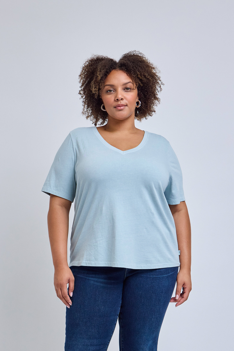 Woman wearing a light blue t-shirt and dark blue jeans against a gray background | model-size: 16