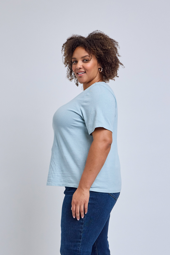 Woman wearing a light blue t-shirt and dark blue jeans on a plain background