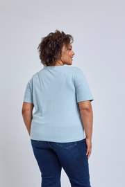 Person wearing a light blue t-shirt and dark blue jeans on a plain background