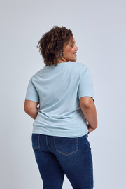 Woman wearing a light blue t-shirt and dark blue jeans on a plain background