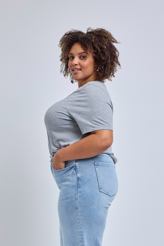 Woman wearing a gray t-shirt and light blue jeans against a plain background