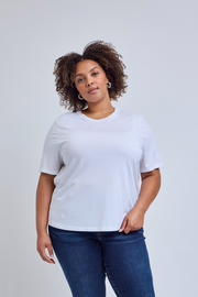 Woman wearing a white t-shirt and dark blue jeans against a light gray background | model-size: 16