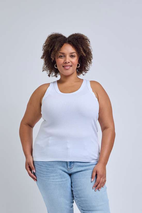Woman wearing a white tank top and light blue jeans against a gray background | model-size: 16