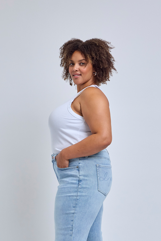 Woman wearing a white tank top and light blue jeans against a plain background