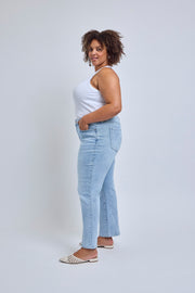 Woman wearing light blue jeans and a white top against a plain background