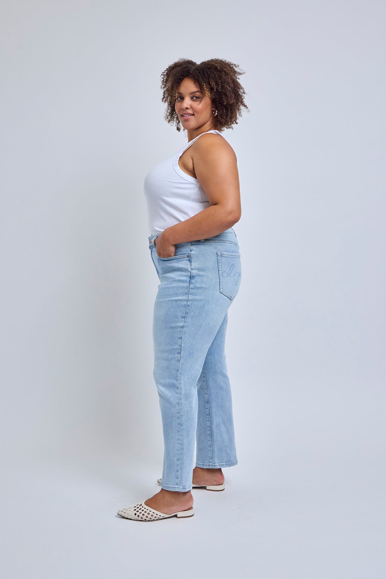 Woman wearing light blue jeans and a white top against a plain background