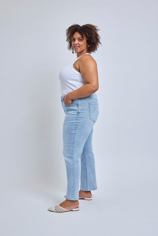 Woman wearing light blue jeans and a white top against a plain background