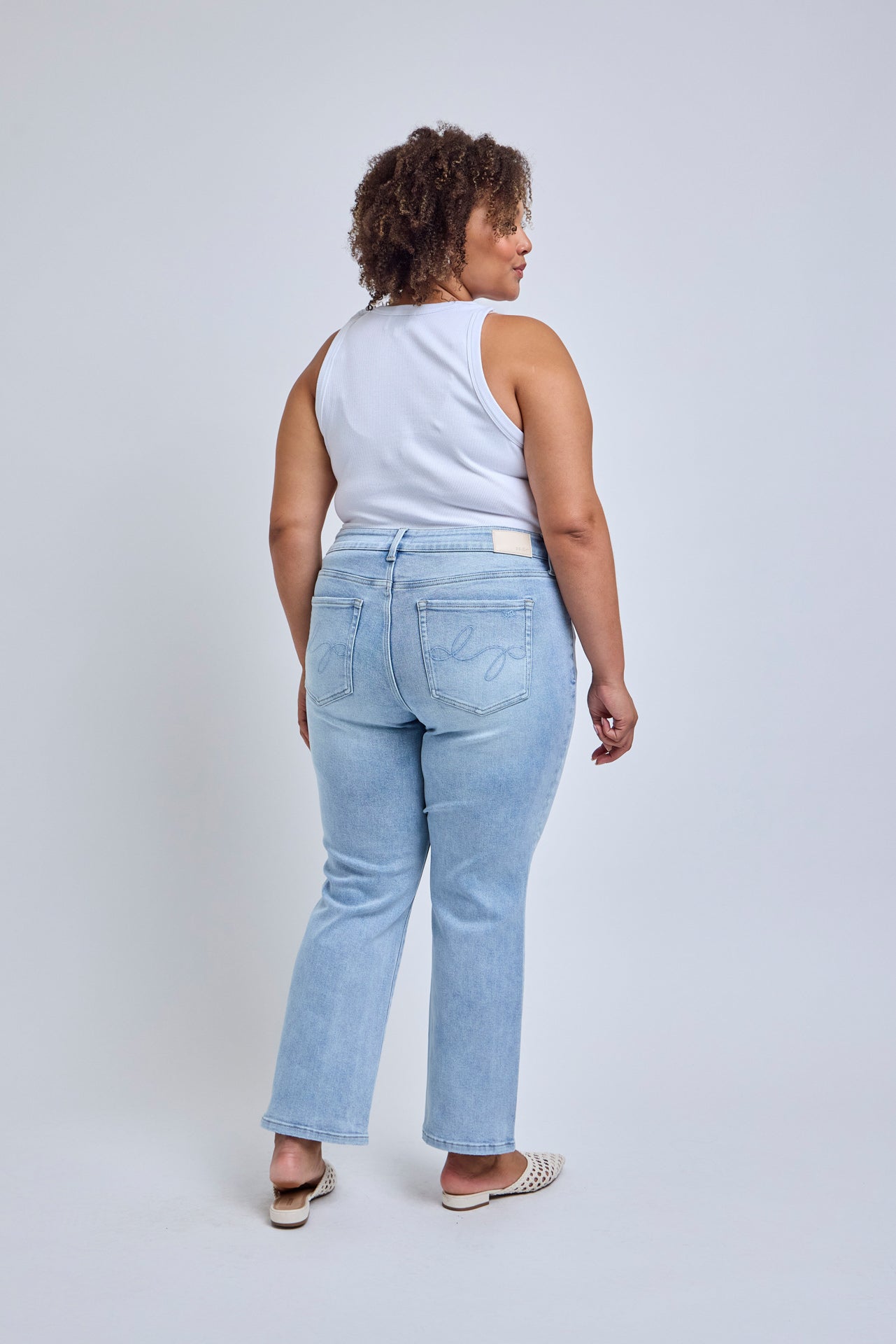 Woman wearing light blue jeans and a white sleeveless top on a plain background