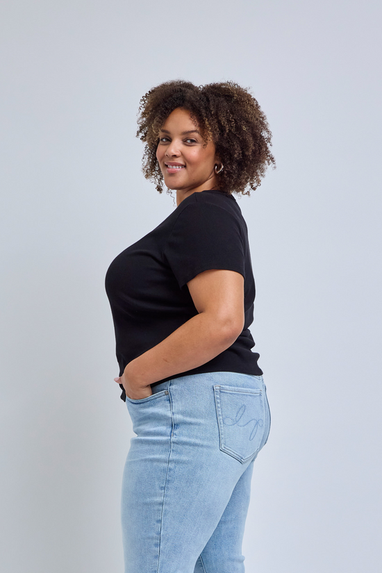 Woman wearing a black t-shirt and light blue jeans against a gray background