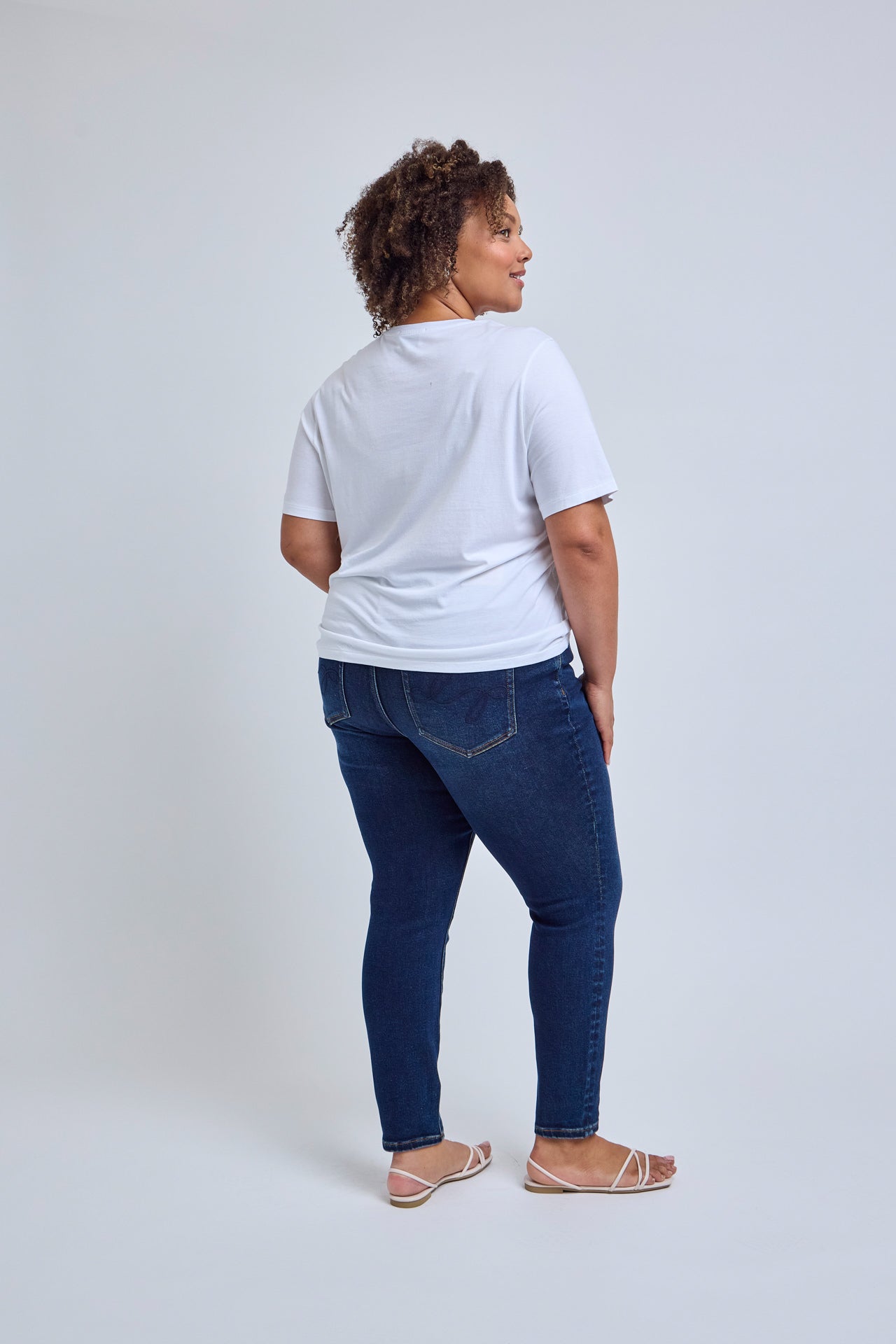 Person wearing a white t-shirt and blue jeans on a light gray background