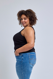 Woman wearing a black tank top and blue jeans against a light gray background