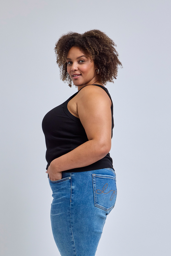 Woman wearing a black tank top and blue jeans against a light gray background