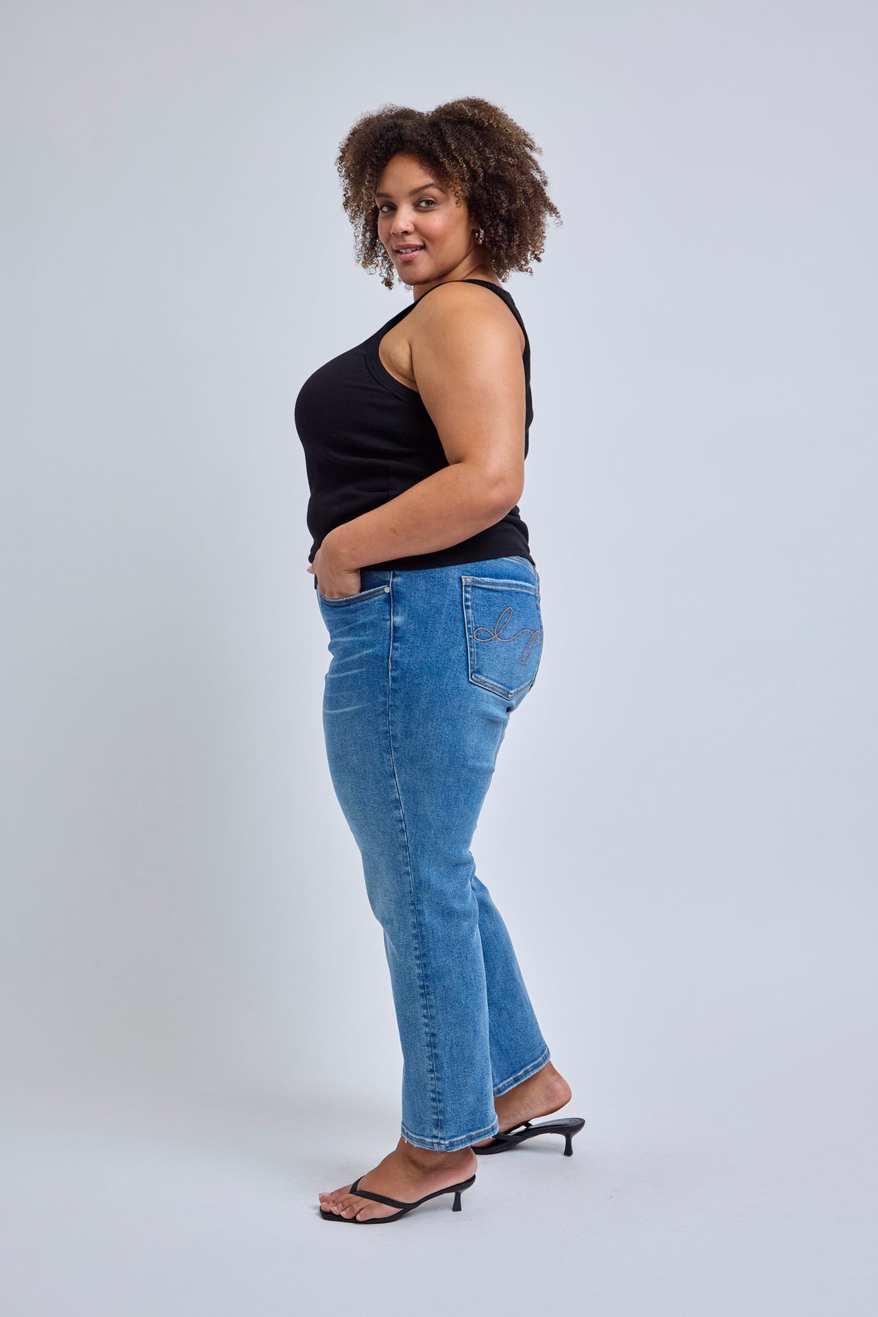Woman wearing blue jeans and a black top on a white background