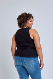 Woman wearing a black sleeveless top and blue jeans on a light gray background