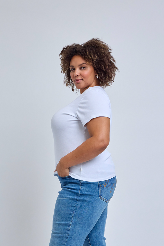 Woman wearing a white t-shirt and blue jeans against a plain background