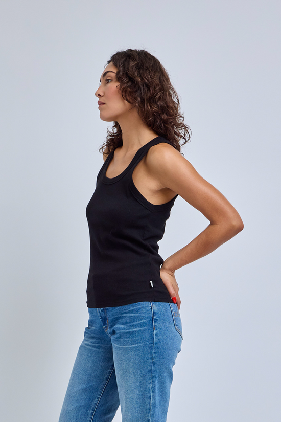 Woman wearing a black tank top and blue jeans against a light gray background