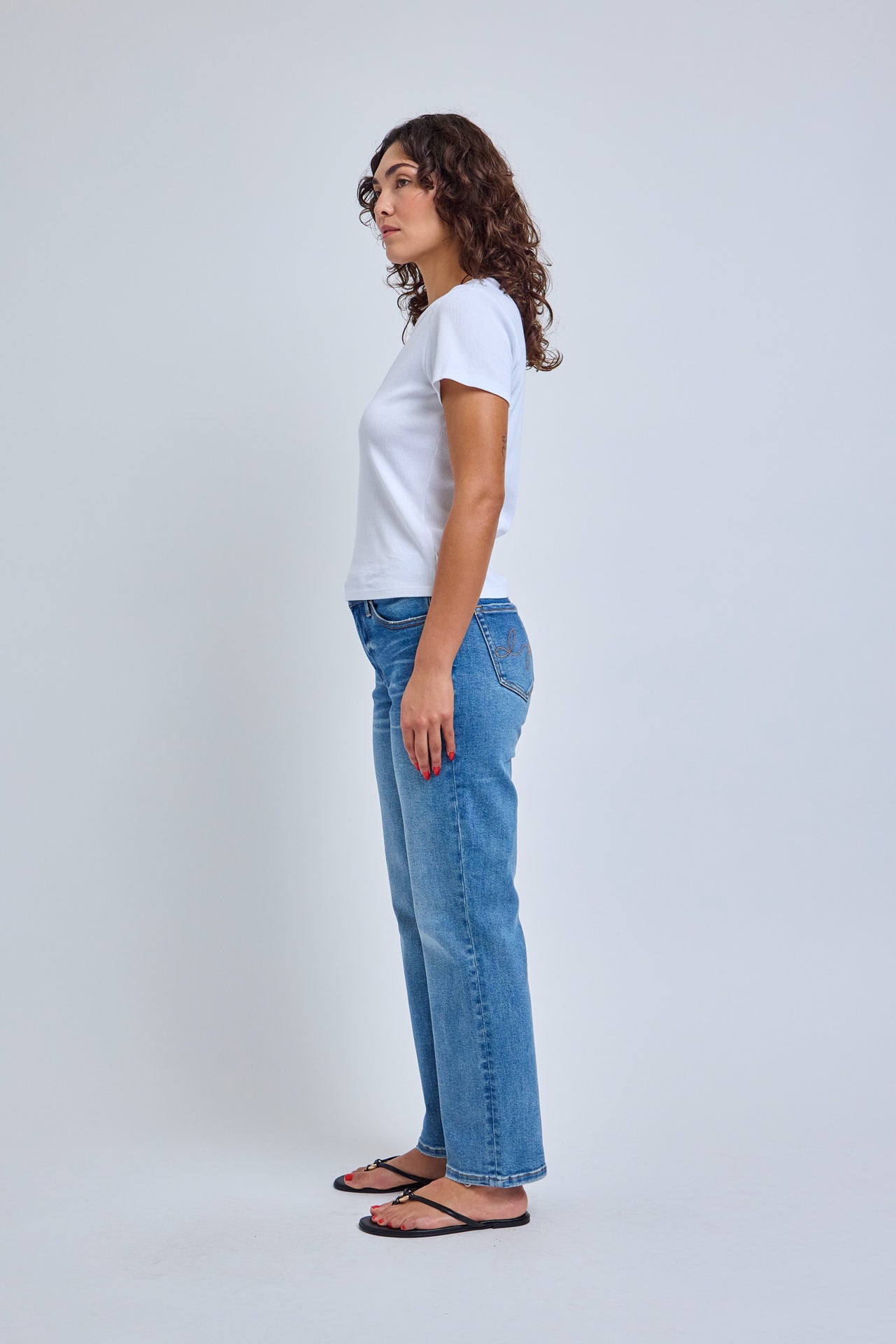 Woman wearing a white t-shirt and blue jeans standing against a plain background