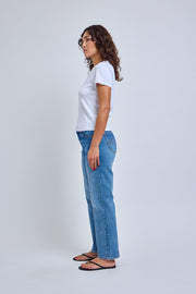 Woman wearing a white t-shirt and blue jeans standing against a plain background